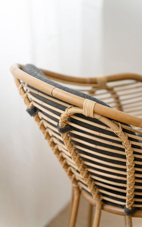 This is a close-up image of Swing Lounge Chair in polished natural rattan. Detail of the curved rattan top rail and plaited back-rest binding.