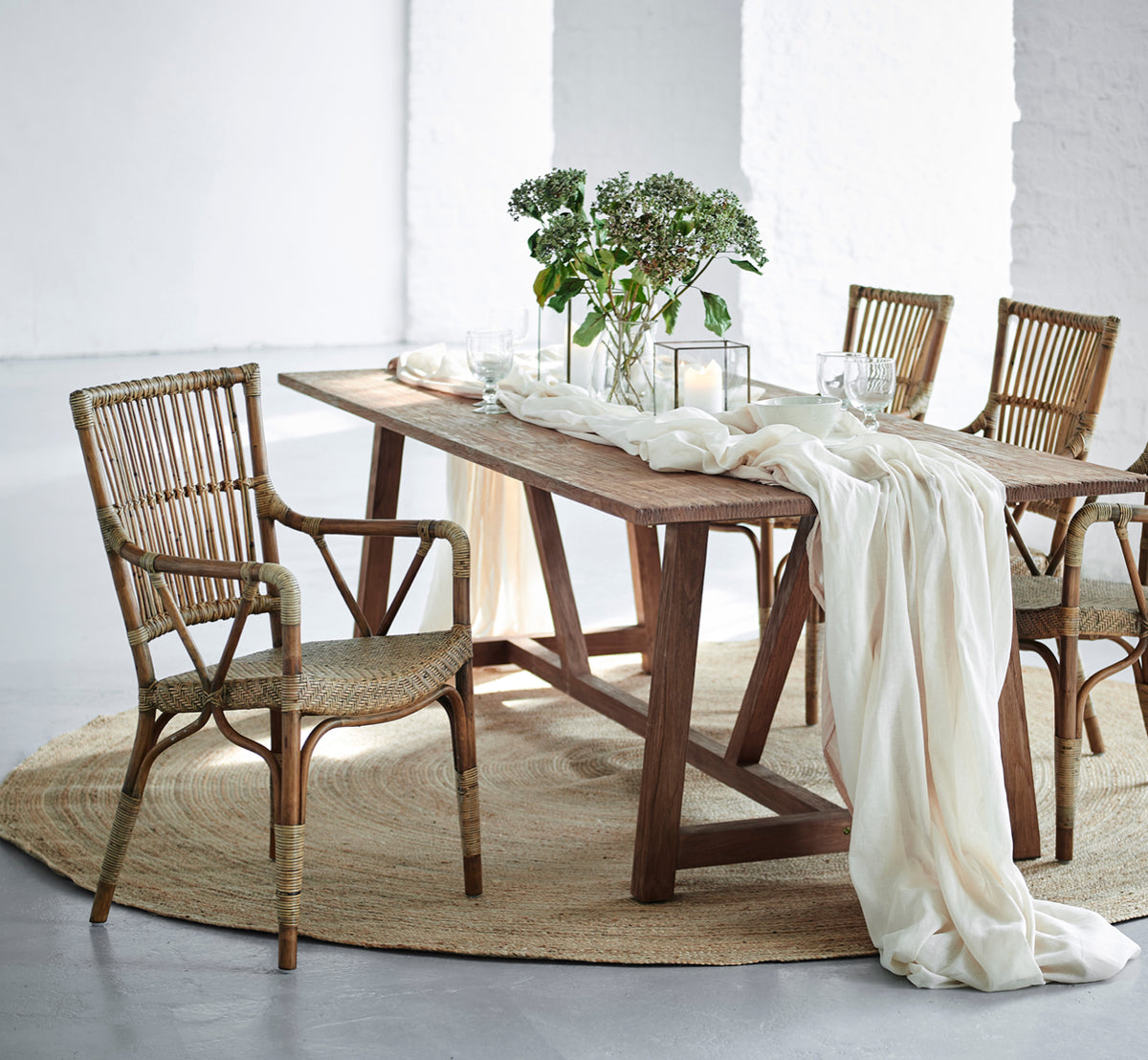 This is a lifestyle image of Piano Dining Chair in antique rattan. Around a rustic wood dining table with linen runner and candles.