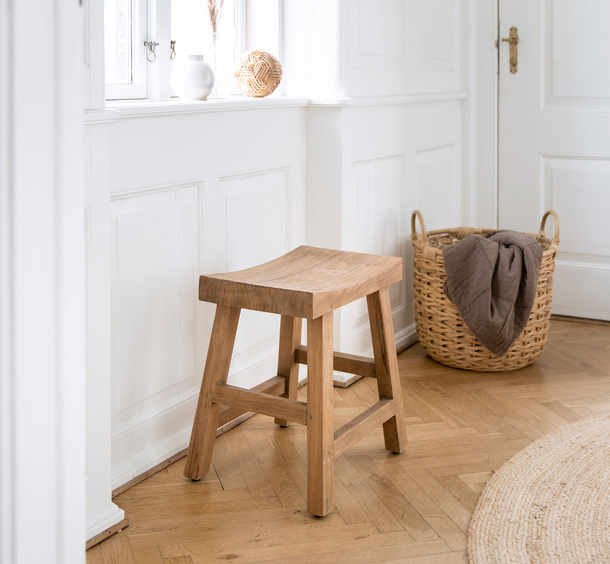This is a lifestyle image of Charles Stool in teak indoor, in a bright white interior with wainscoting and herringbone parquet.