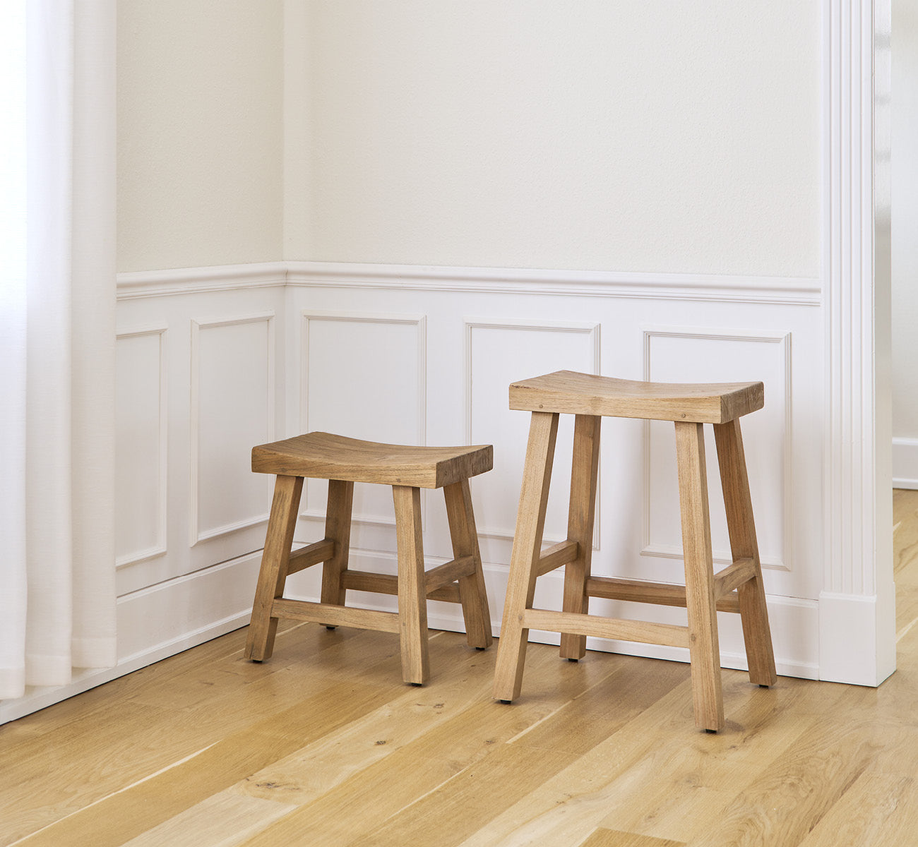 This is a lifestyle image of Charles Stool in teak indoor, in a bright white interior with wainscoting and herringbone parquet.