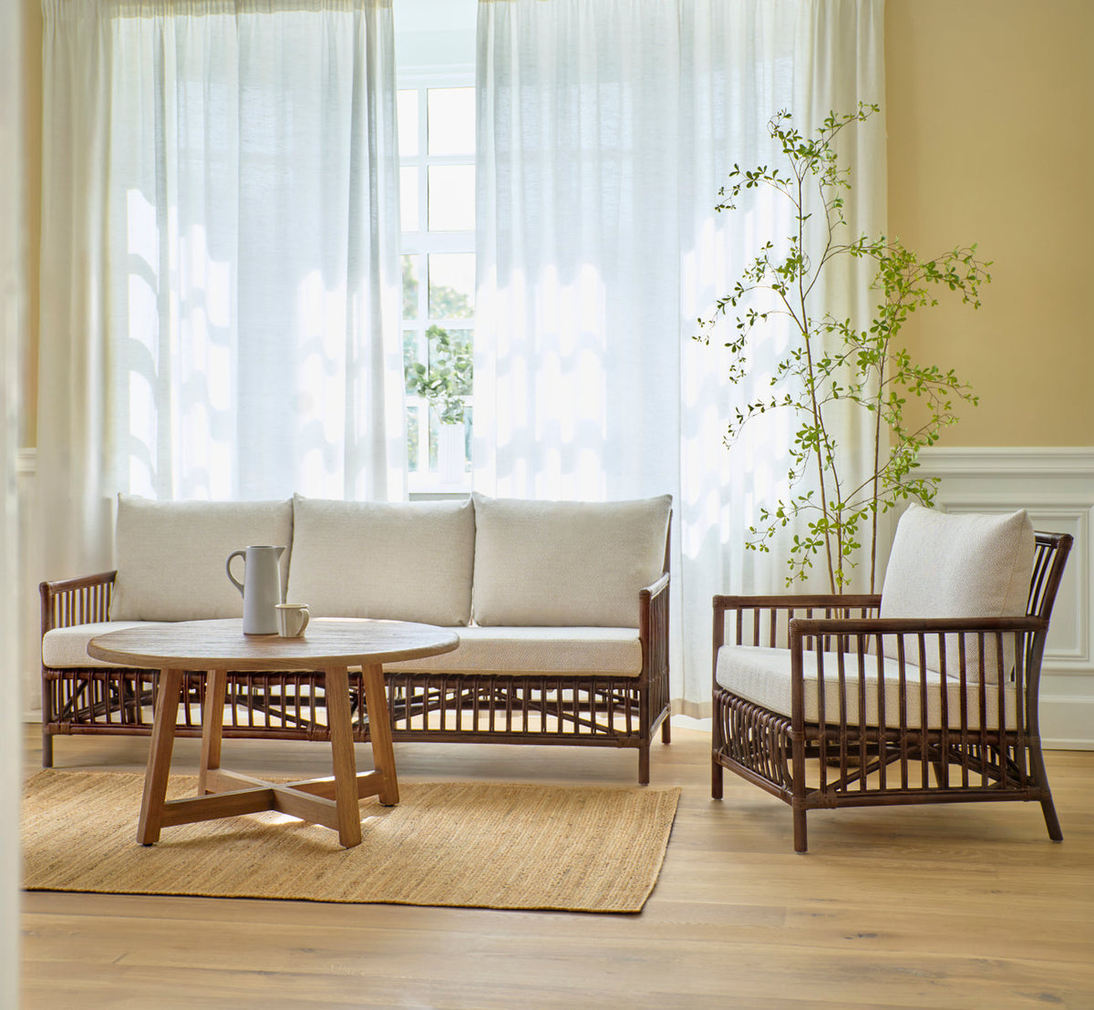 This is a lifestyle image of Caroline Sofa in brown rattan. With lounge chair and teak coffee table on a jute rug.