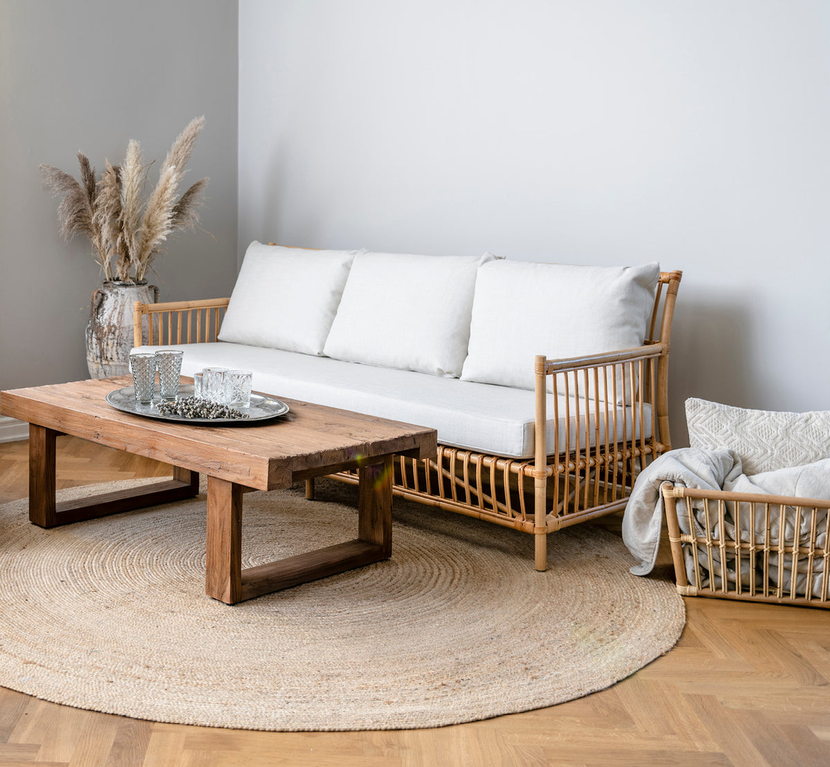 This is a lifestyle image of Caroline Sofa in natural rattan, in a bright interior with white panelled walls and herringbone parquet.