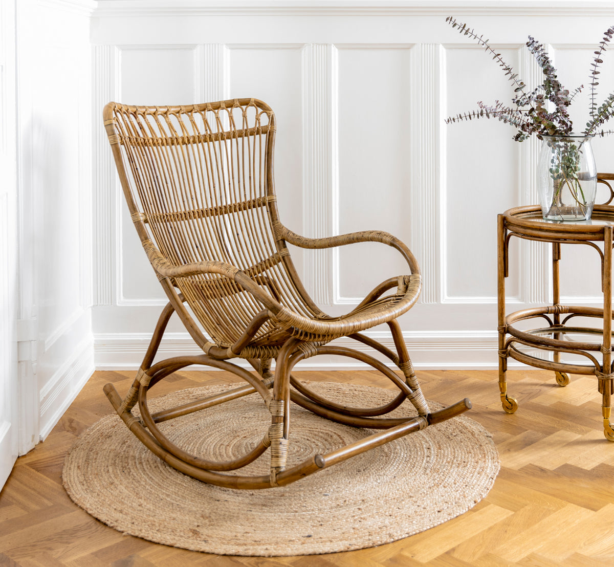 This is a lifestyle image of Romeo Trolley in antique rattan. Styled with hydrangeas and ceramics against a white brick wall.