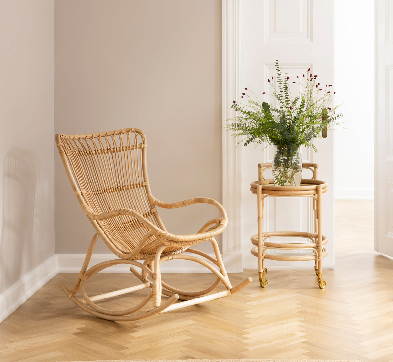 This is a lifestyle image of Romeo Trolley in natural rattan. Styled with glasses in a cozy corner with herringbone parquet floor.