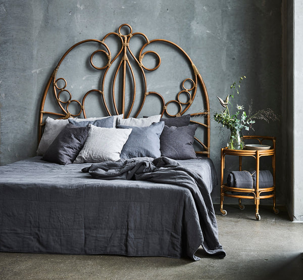 This is a lifestyle image of Natalia Headboard in antique rattan, in a serene bright bedroom with neutral linen and herringbone parquet.