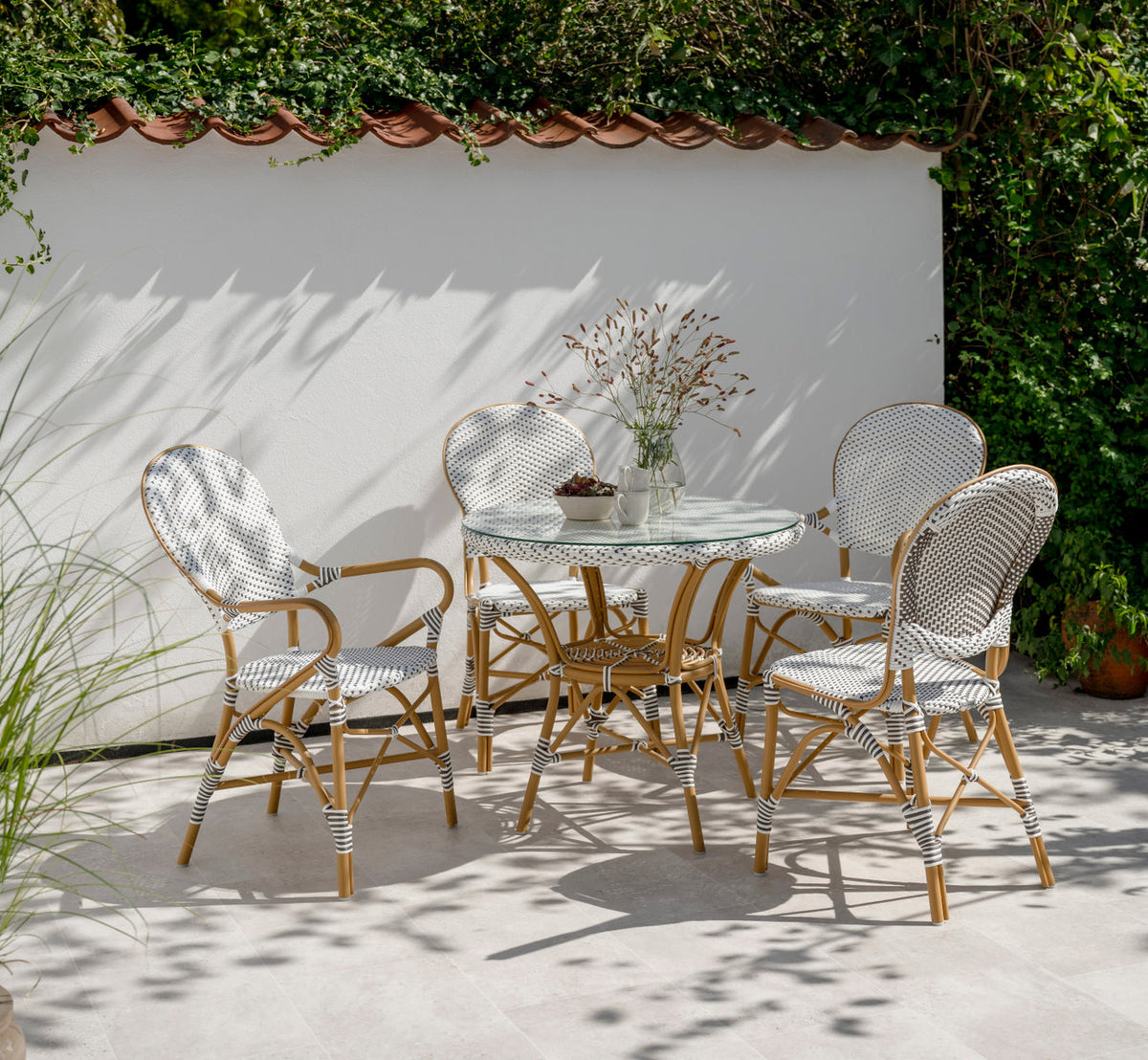 This is a lifestyle image of Isabell Exterior Dining Chair in almond aluminium frame white w cappuccino dot artfibre. On a sunny walled terrace.