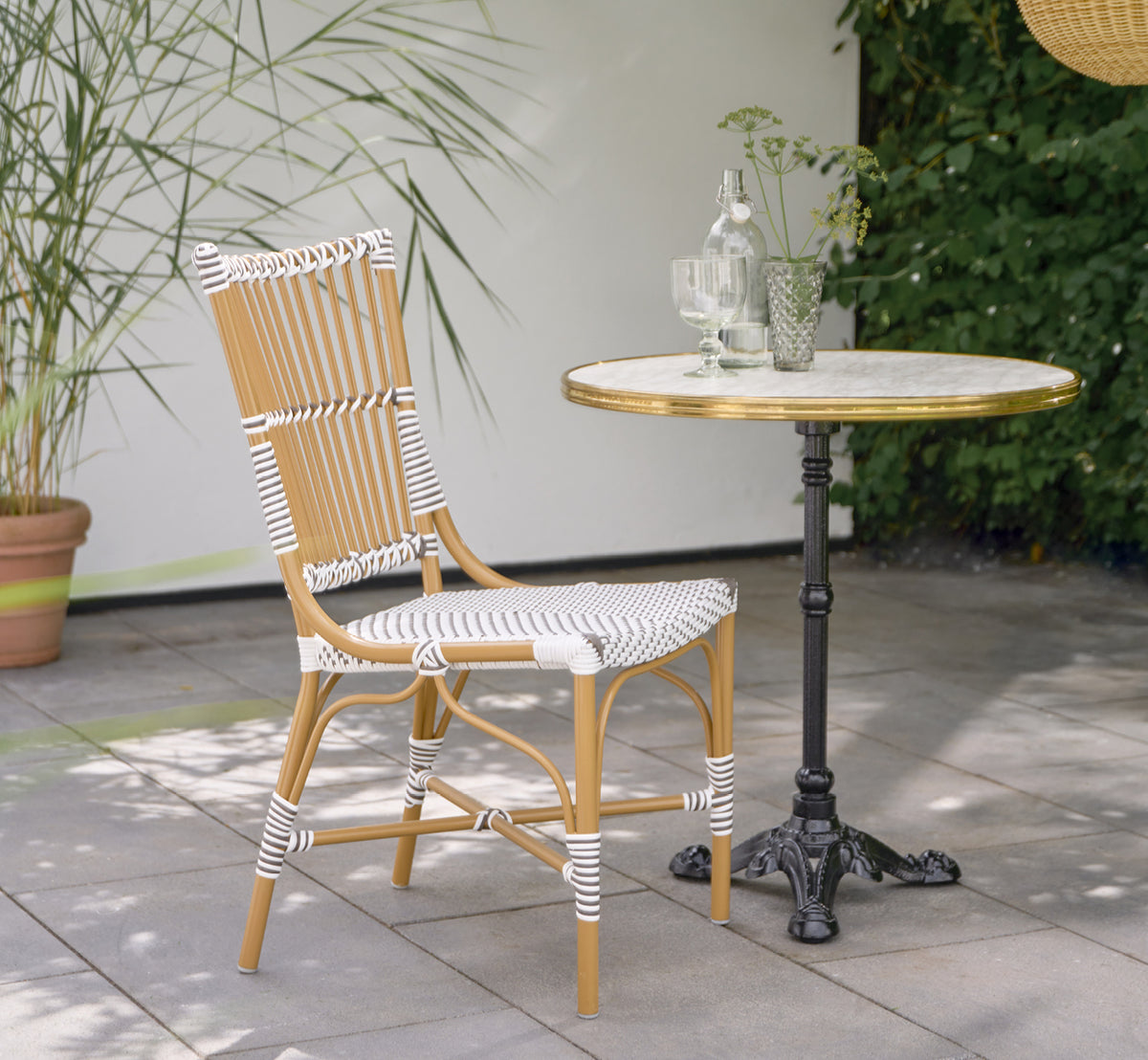 This is a lifestyle image of Monique Exterior Dining Chair in white w cappuccino dot ArtFibre. On a sunny terrace with palms.