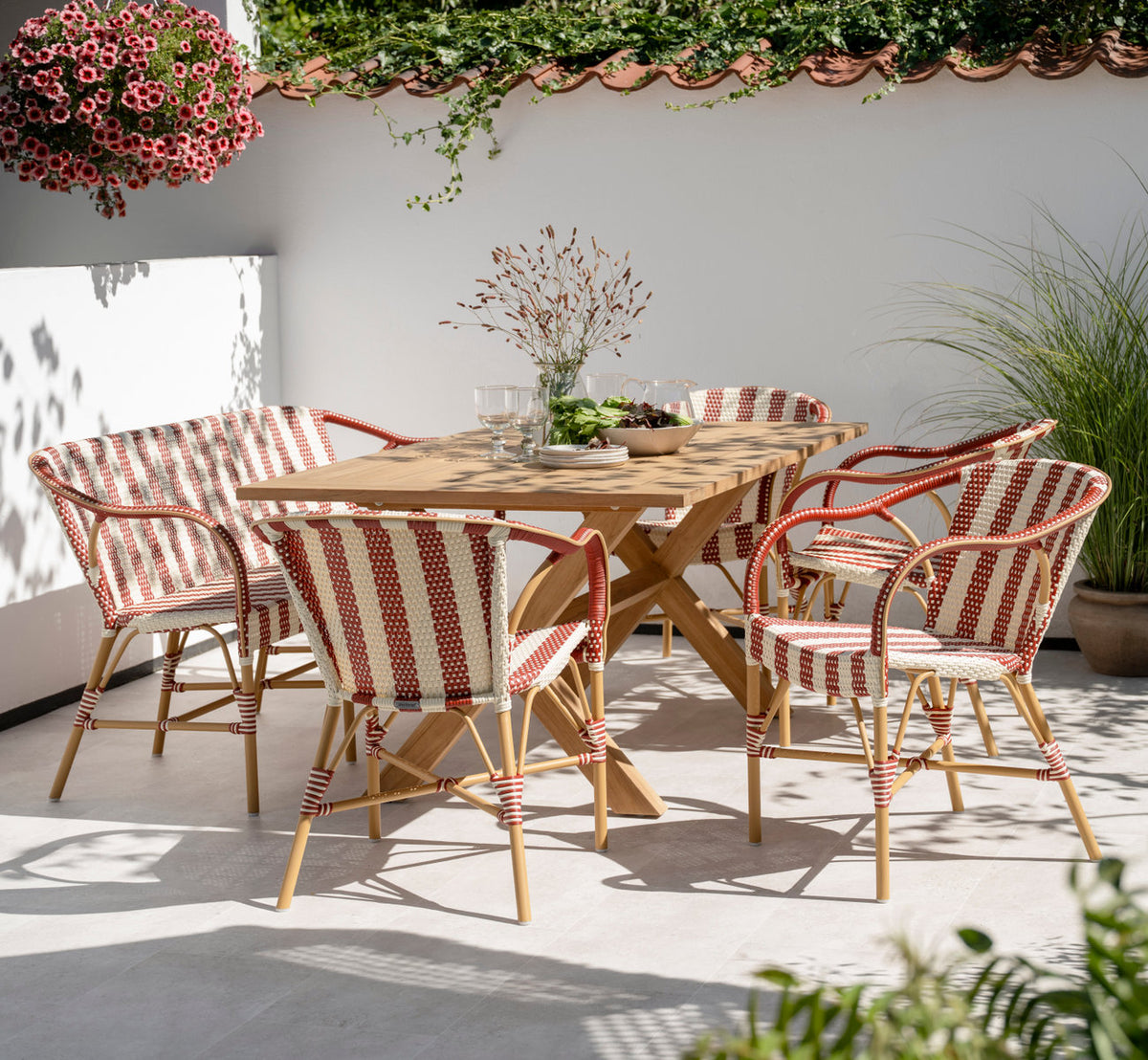 This is a lifestyle image of Madeleine Exterior Dining Chair in almond aluminum frame striped ivory burgundy. At a teak table on a sunny terrace.