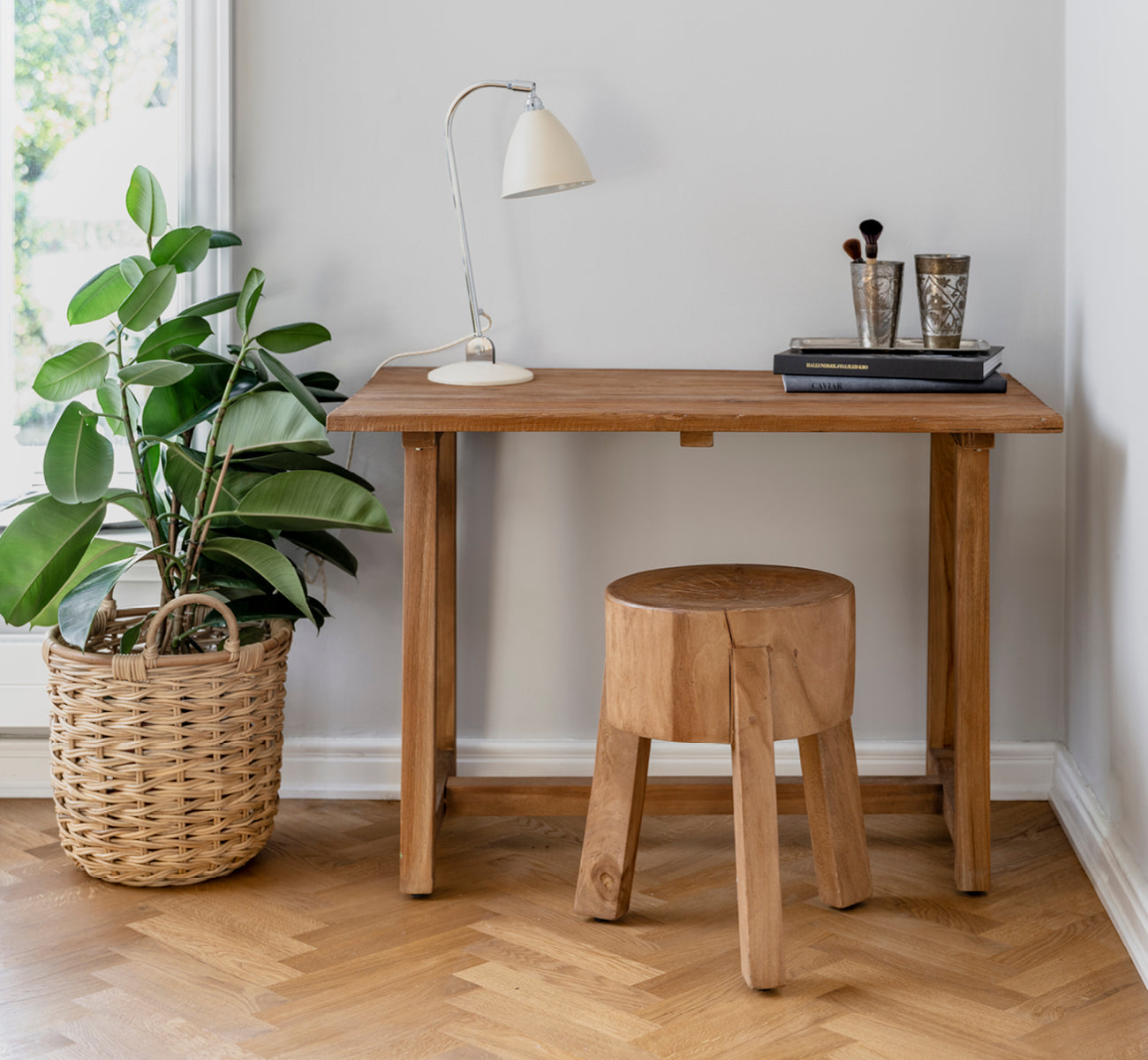 This is a lifestyle image of Roger Stool in teak indoor. Placed at a wooden desk with lamp and plant in a bright herringbone-floor study.