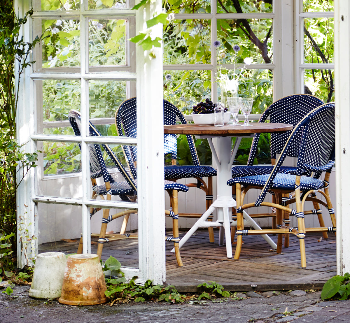 This is a lifestyle image of Sofie Dining Chair in navy blue w white dot artfibre skin on natual rattan frame. Styled in a bright interior setting.
