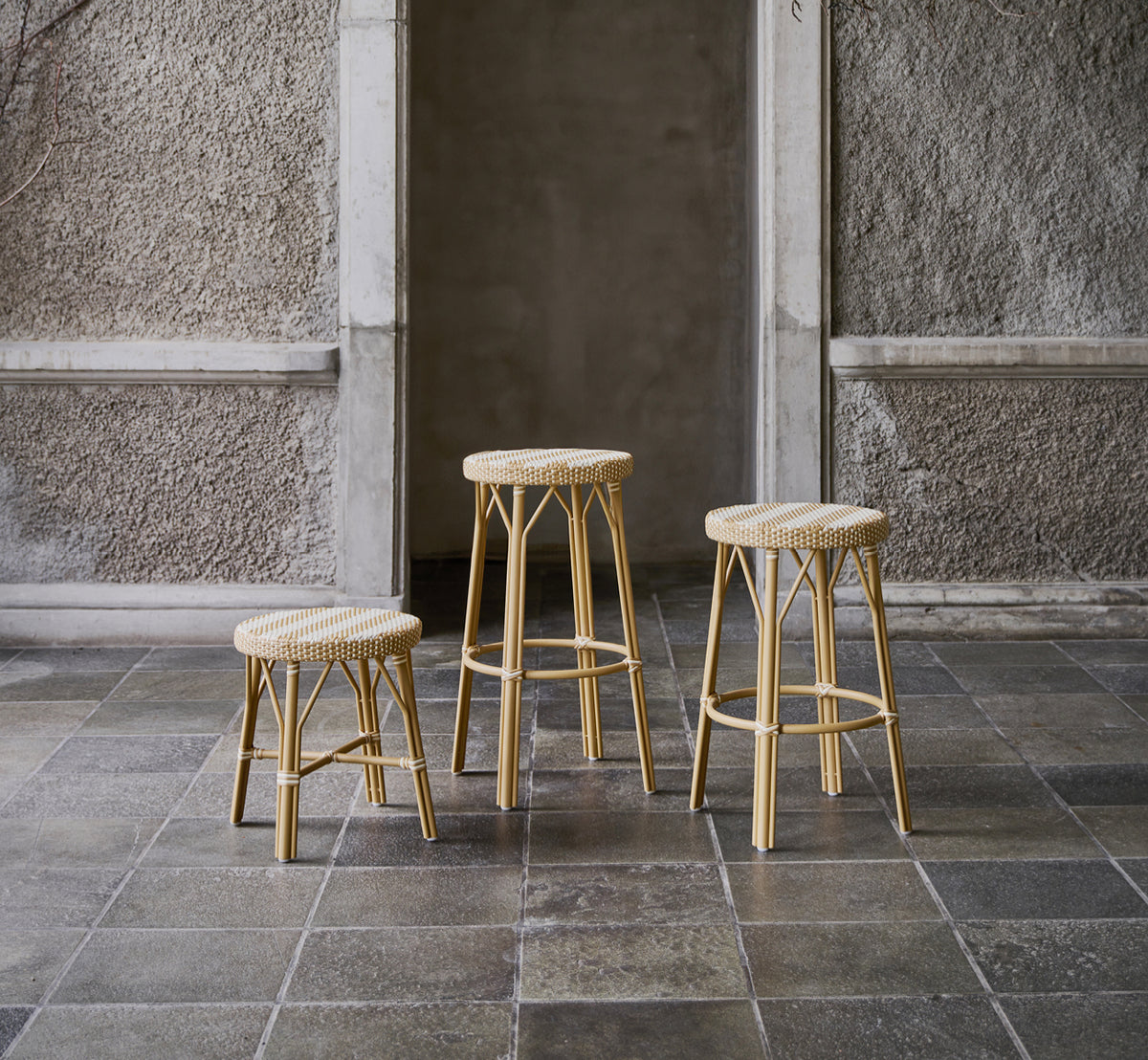 This is a lifestyle image of Simone Counter Stool in striped honey ivory ArtFibre Skin on Rattan frame. Shown in a stone courtyard.