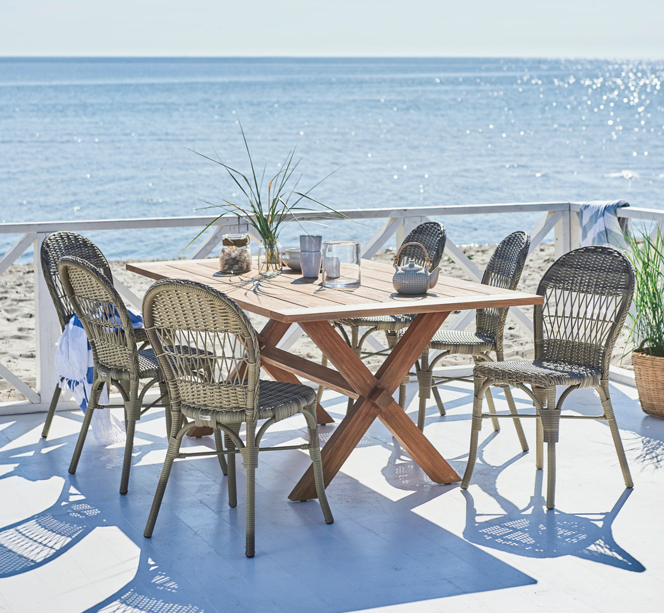 This is a lifestyle image of Ofelia Exterior Chair in antique grey artfibre aluminium. On a beach deck with ocean view and teapot.