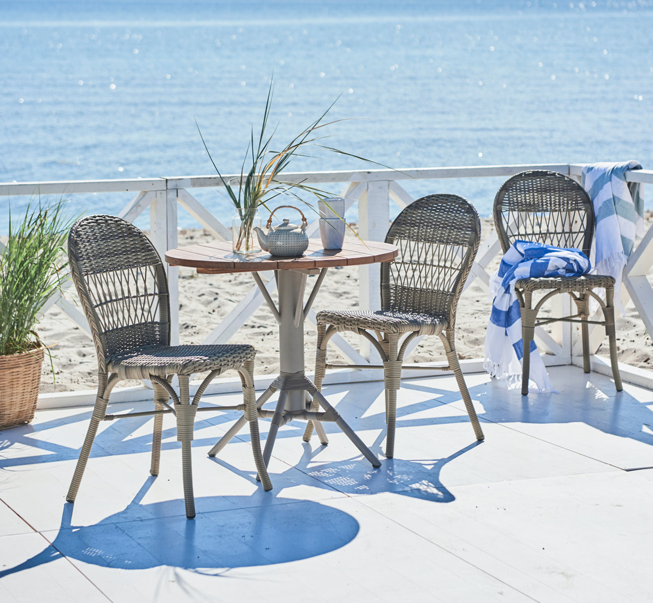 This is a lifestyle image of Ofelia Exterior Chair in antique grey artfibre aluminium. On a seaside deck with white railing and towel.