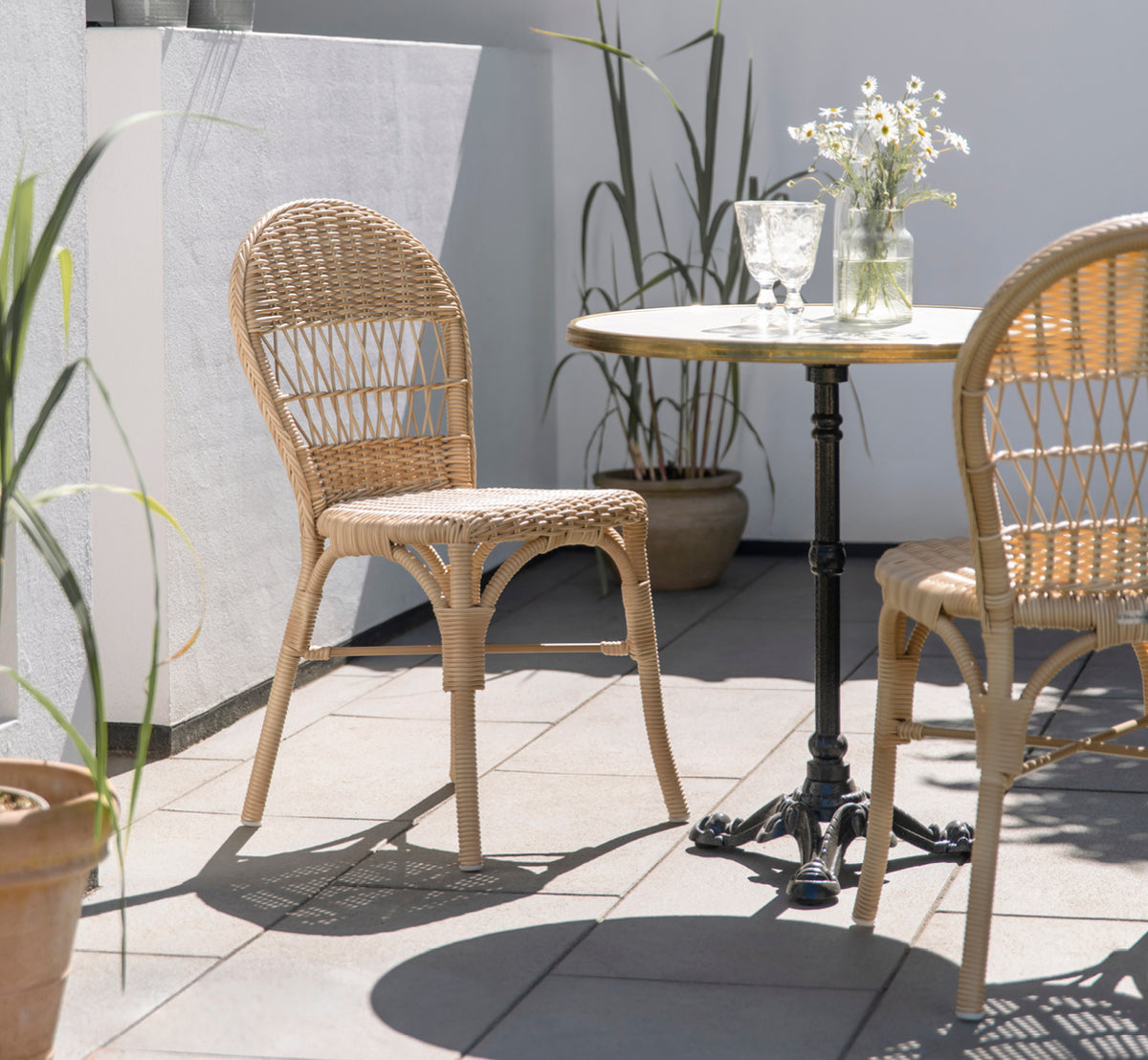 This is a lifestyle image of Ofelia Exterior Chair in natural artfibre aluminium. On a sunny patio with daisies and bistro table.