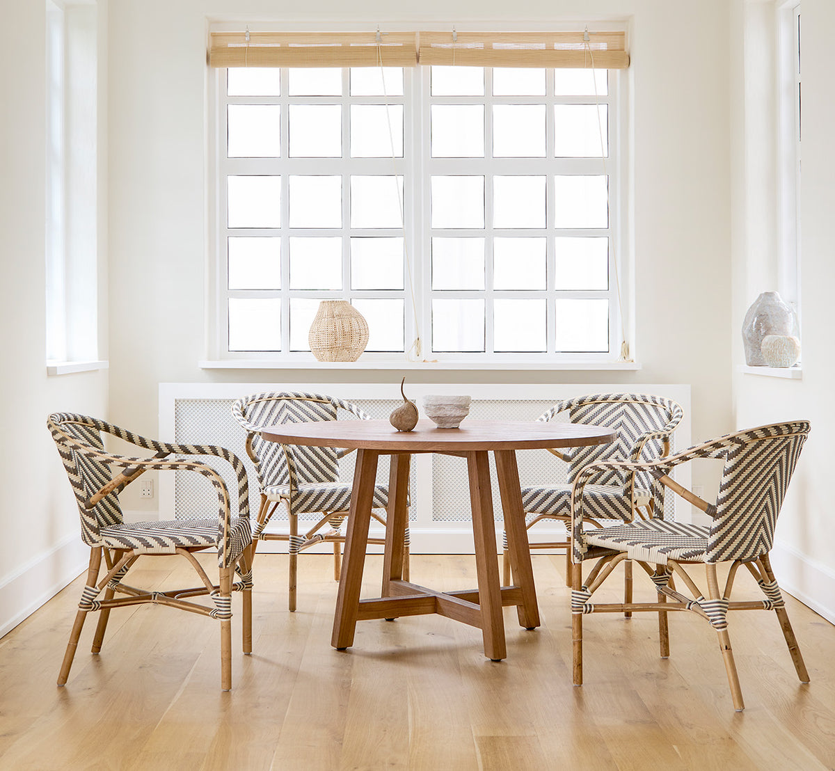 This is a lifestyle image of Aksel Dining Table in teak indoor, in a bright dining area with large windows and light wood flooring.