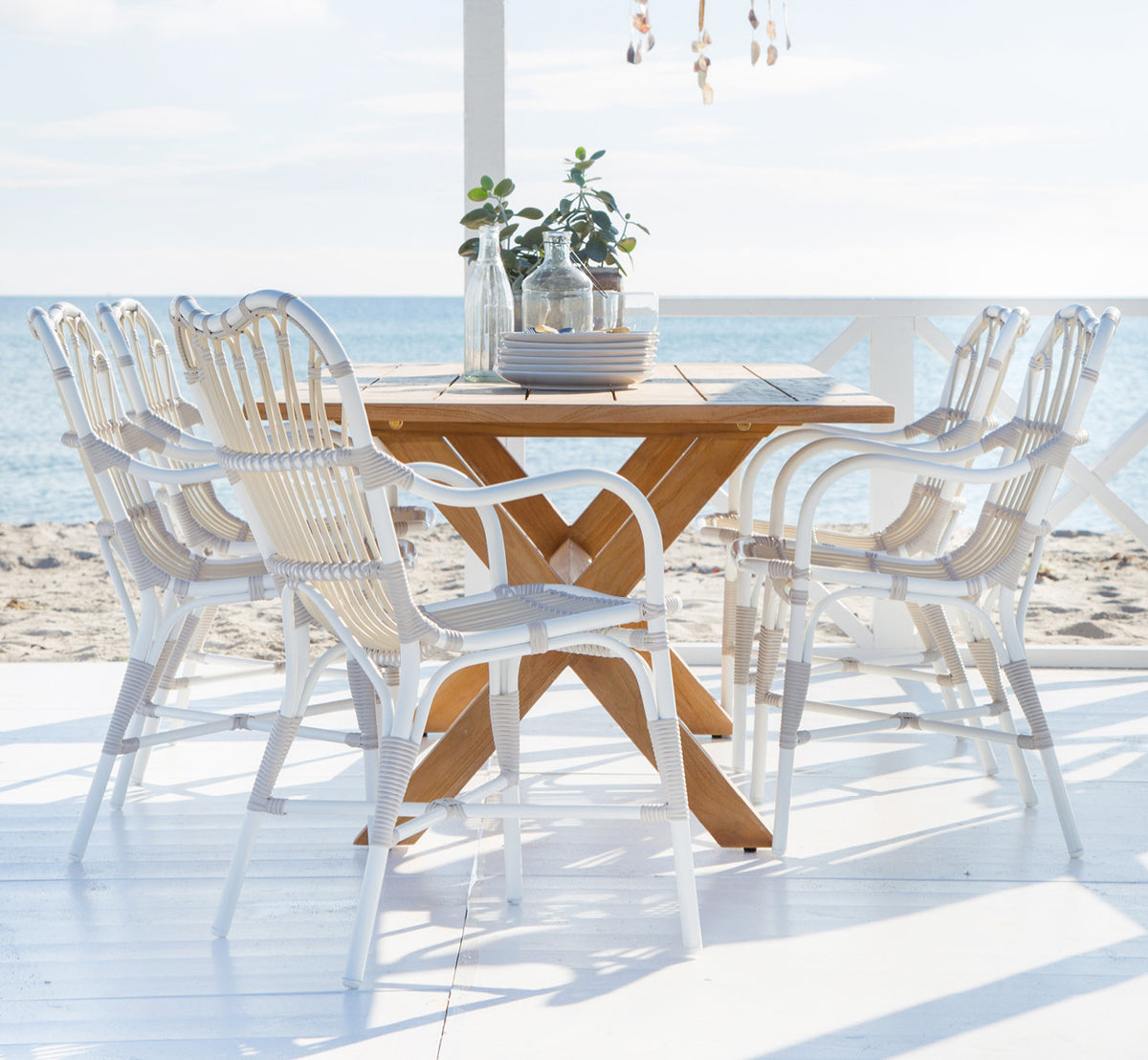 This is a lifestyle image of Colonial Table 160 in outdoor Teak, on a beachside terrace with white wooden decking and sea views.