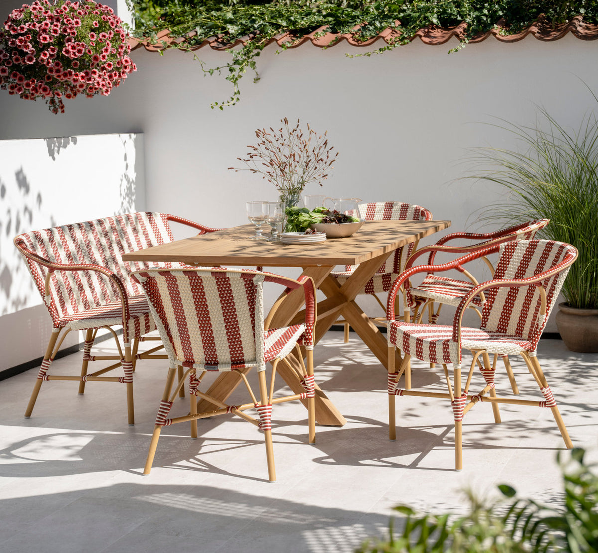 This is a lifestyle image of Colonial Teak Table 160x100 cm in teak outdoor. With striped chairs on a sunny walled terrace.