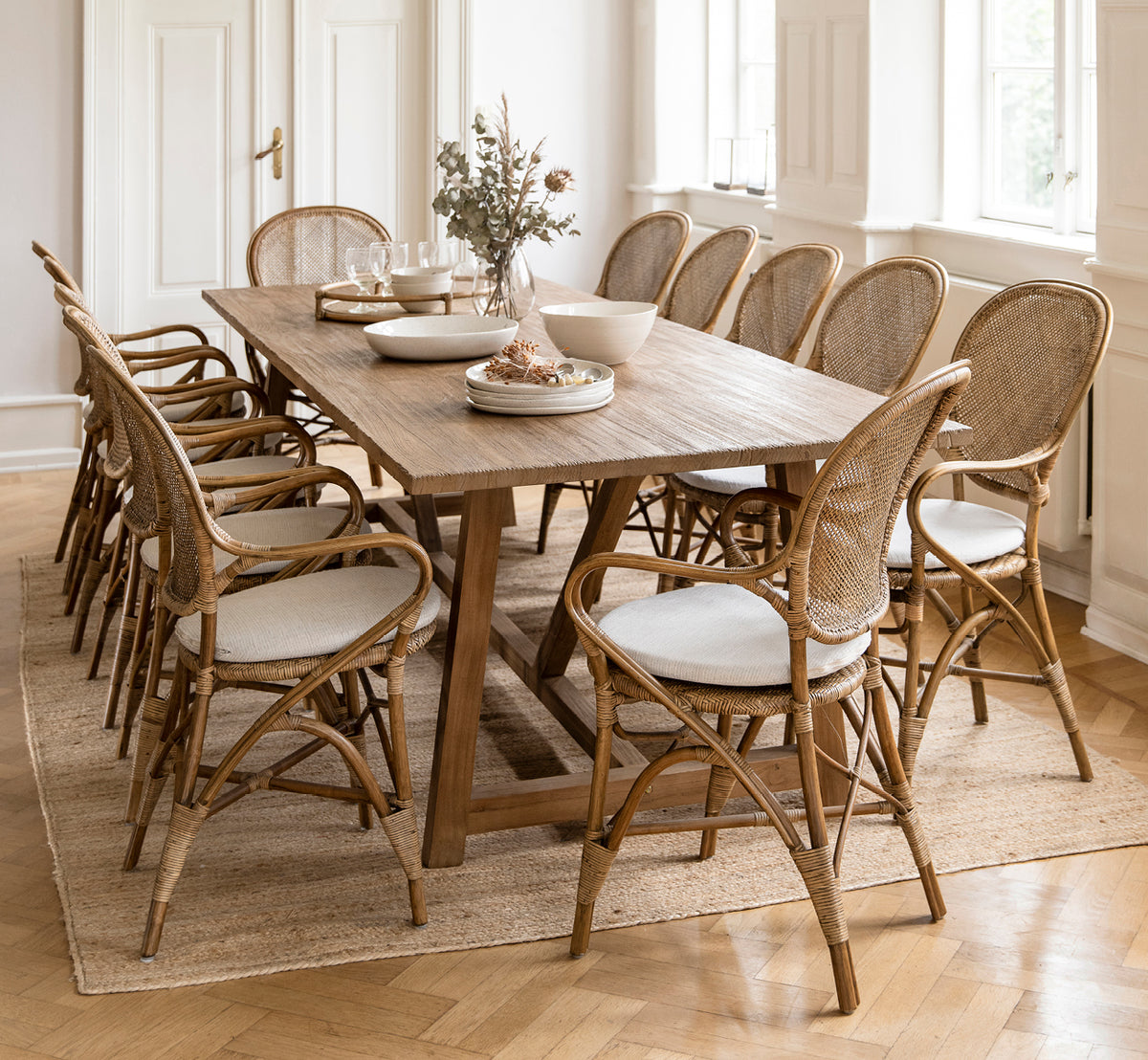 This is a lifestyle image of Lucas Teak Dining Table 300X100 cm in teak indoor. Set for dining with rattan chairs in an elegant paneled room.