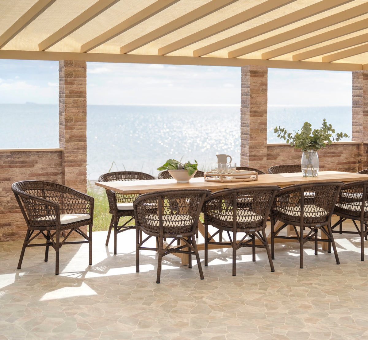 This is a lifestyle image of George Teak Extendable Table 200-280x100 cm in teak outdoor. Long dining setting on a terrace by the sea.