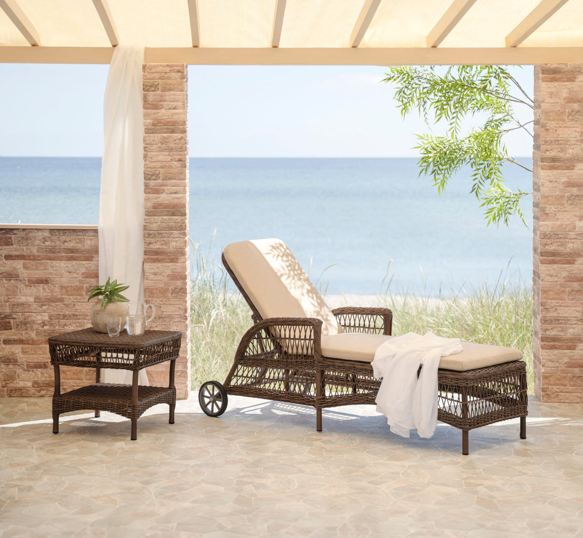 This is a lifestyle image of Susy Exterior Side Table in brown artfibre aluminum. With a white towel on a terrace by the sea.