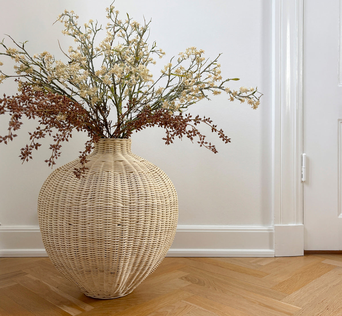 This is a lifestyle image of Flumen Basket in natural core weave iron frame, in a bright white interior with wainscoting, styled with dried flowers.