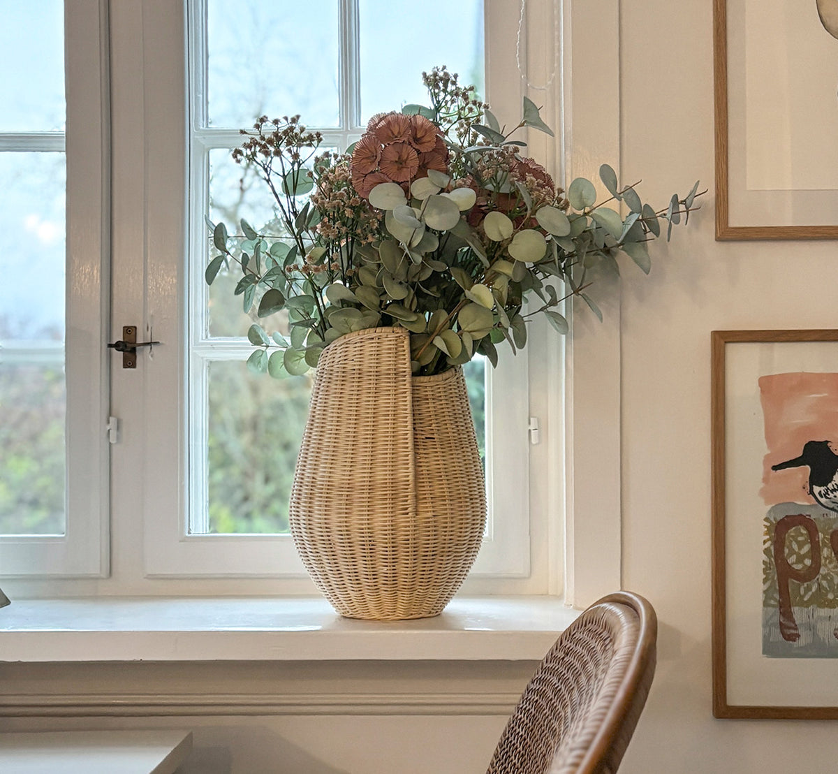 This is a lifestyle image of Aura Basket in natural core weave Iron frame, in a bright white interior with wainscoting, styled with dried flowers.