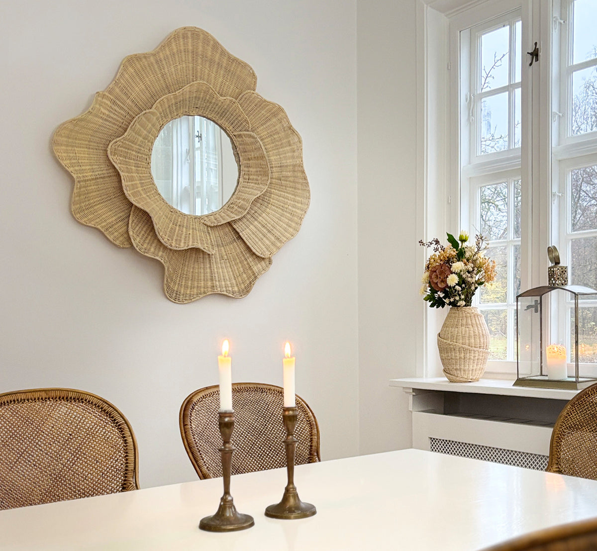 This is a lifestyle image of Floral Mirror in natural core weave iron frame, hung in a bright dining room with candlesticks and natural window light.