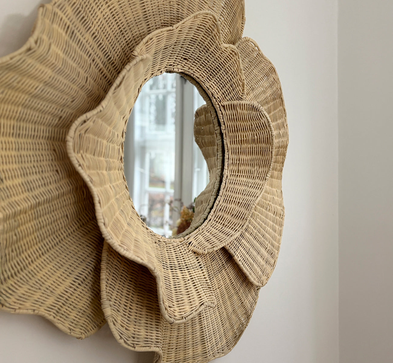 This is a lifestyle image of Floral Mirror in natural core weave iron frame, hung in a bright dining room with candlesticks and natural window light.