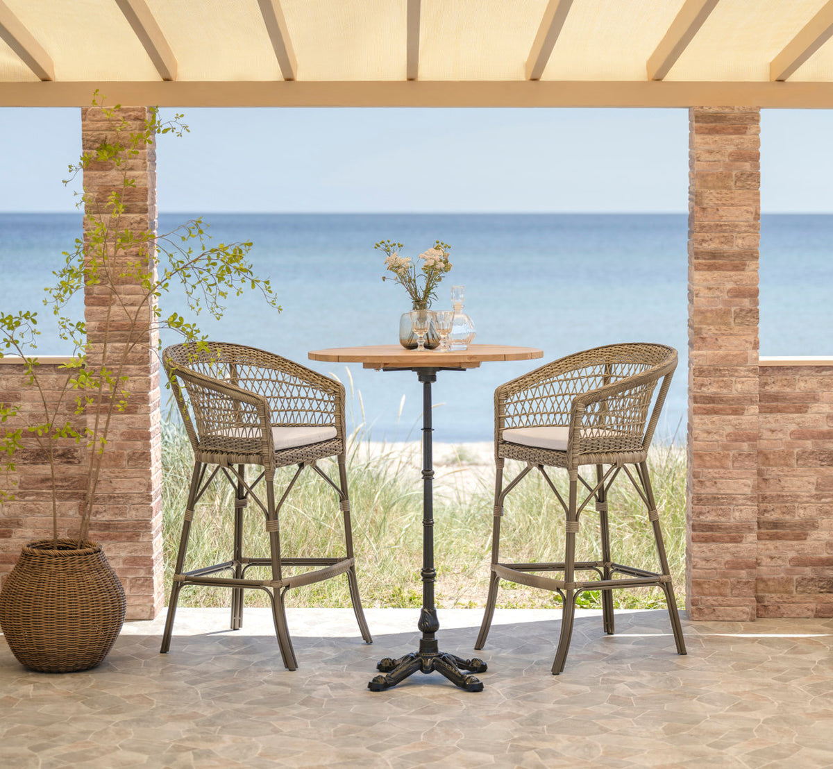 This is a lifestyle image of Lyon Bar Table-Teak Ø80 cm in cast iron. Bar setting with sea view.