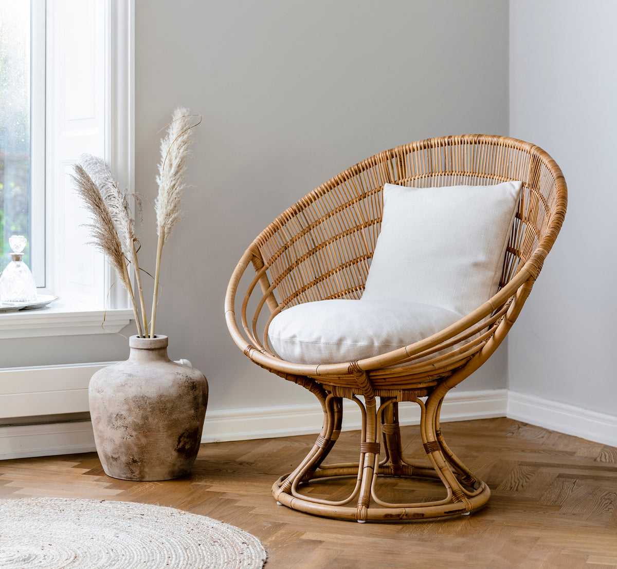This is a lifestyle image of Luna Lounge Chair in natural skin on rattan. Styled with a white cushion in a cozy corner with pampas grass décor.