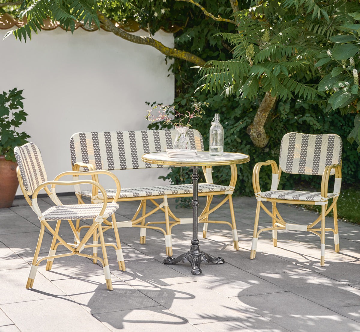 This is a lifestyle image of Bistro Exterior Chair in natural Aluminium ArtFibre, in an outdoor garden café with a bistro table and surrounding trees.