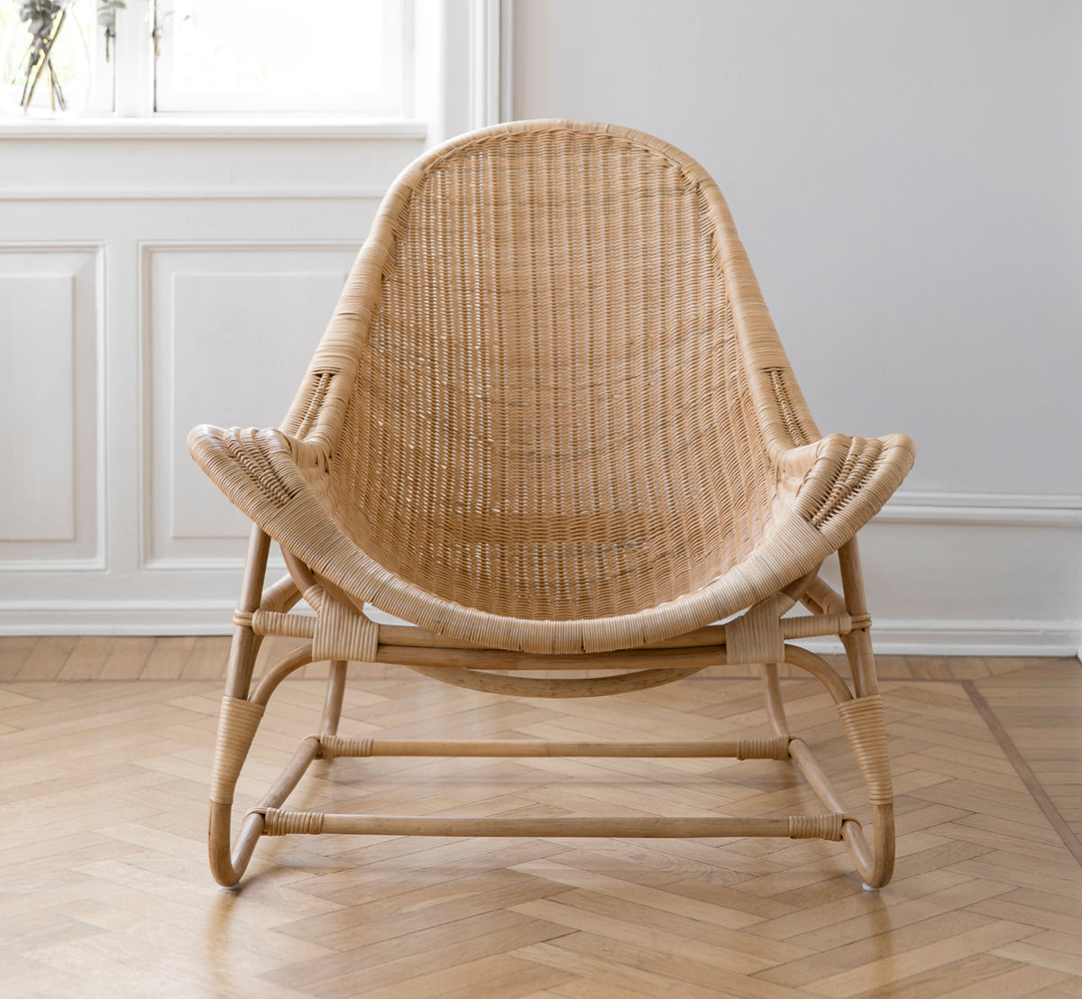This is a lifestyle image of Pacifique Lounge Chair in natural core weave rattan frame. Styled in a bright interior setting.