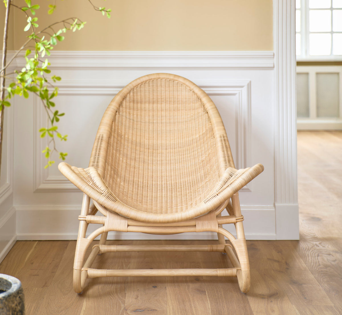 This is a lifestyle image of Pacifique Lounge Chair in natural core weave rattan frame. Front view by white paneled walls.