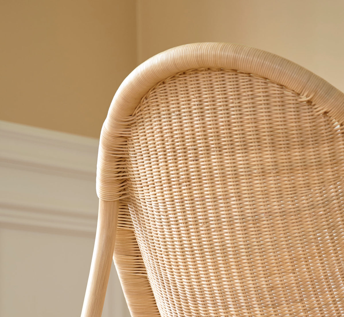 This is a lifestyle image of Pacifique Lounge Chair in natural core weave rattan frame. Woven back in soft light by a paneled wall.