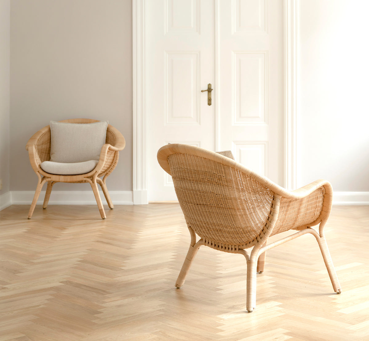 This is a lifestyle image of Madame Lounge Chair in natural core weave rattan frame. Bright room with herringbone floor and white double doors.