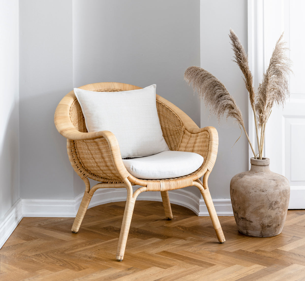 This is a lifestyle image of Madame Lounge Chair in natural core weave rattan frame. Cozy corner with herringbone floor and pampas grass vase.