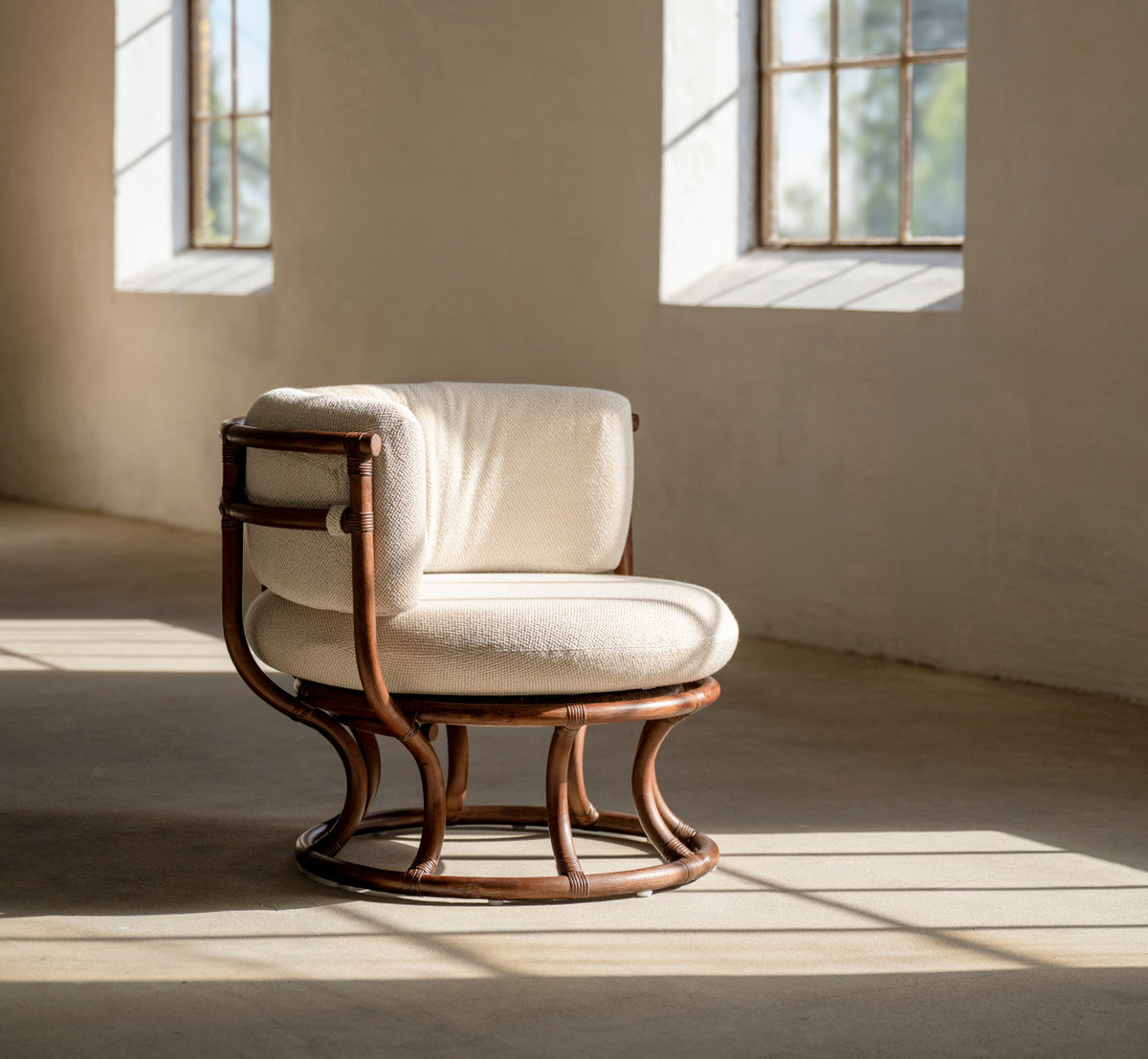 This is a lifestyle image of Coco Lounge Chair in brown rattan. With cream cushions in a sunlit room.
