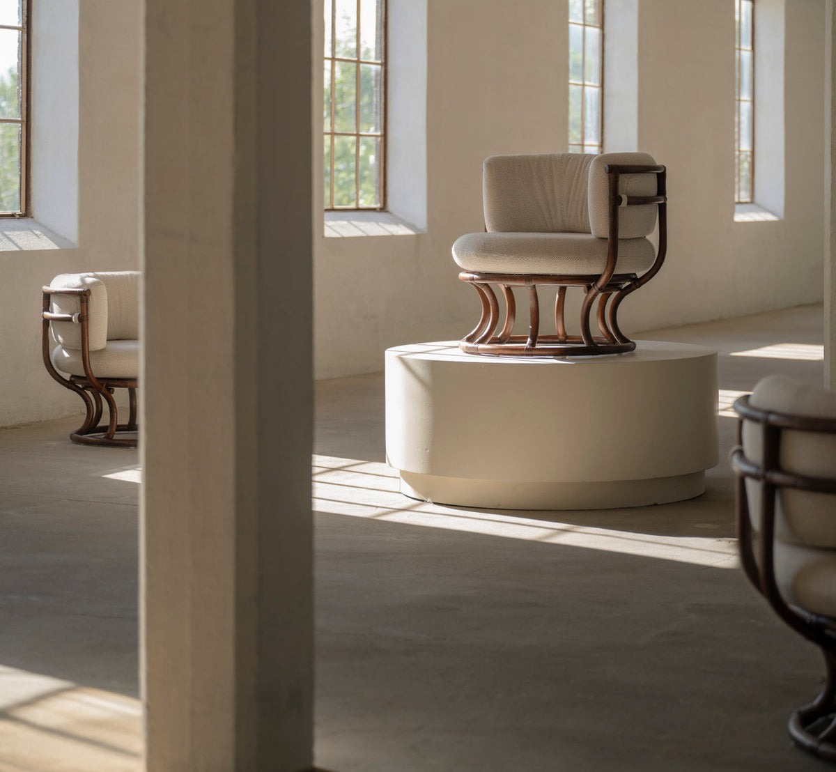 This is a lifestyle image of Coco Lounge Chair in brown rattan. On a white plinth in a sunlit gallery.
