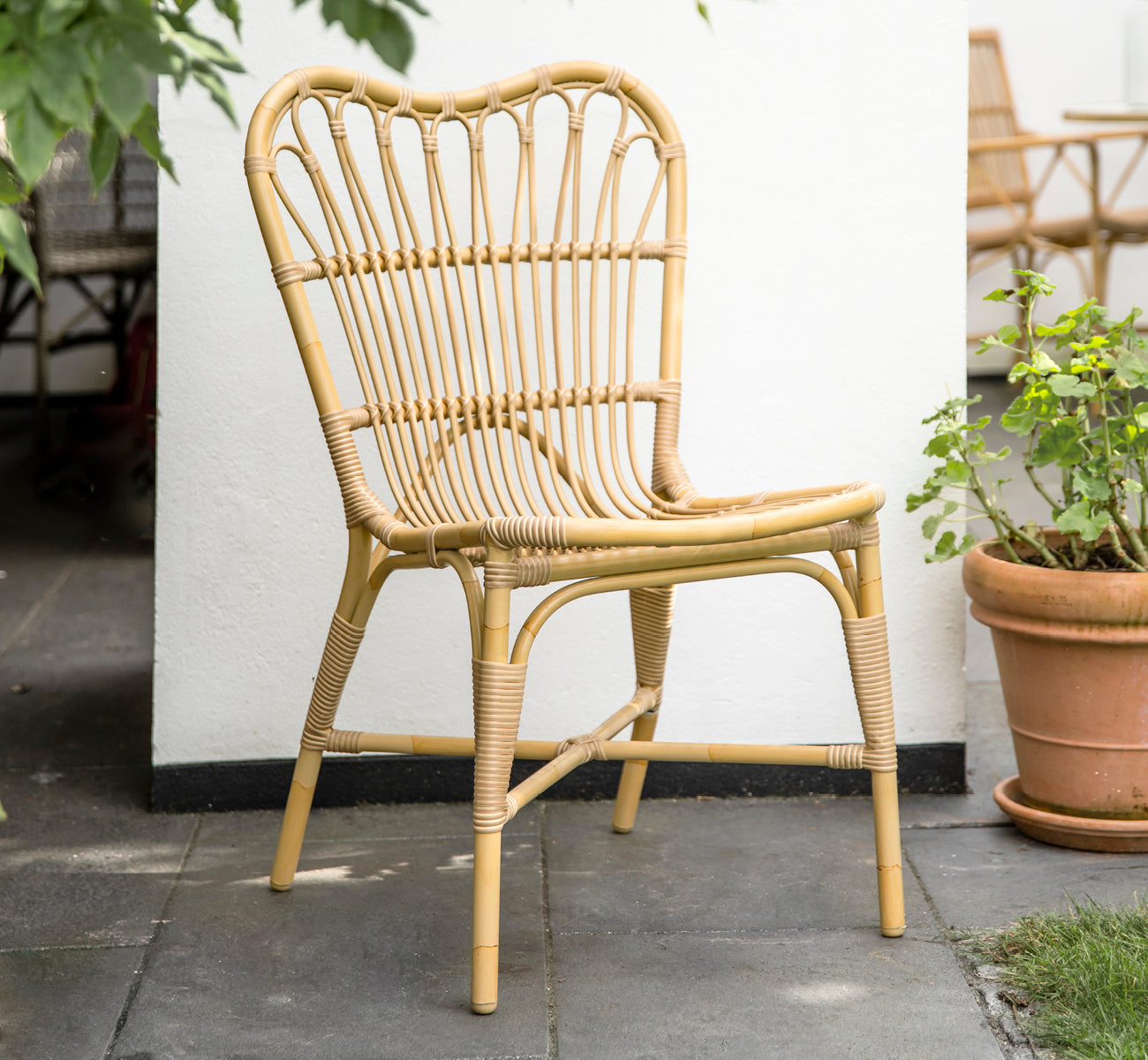This is a lifestyle image of Margret Exterior Side Chair in natural aluminium artfibre. White courtyard with terracotta pots and plants.