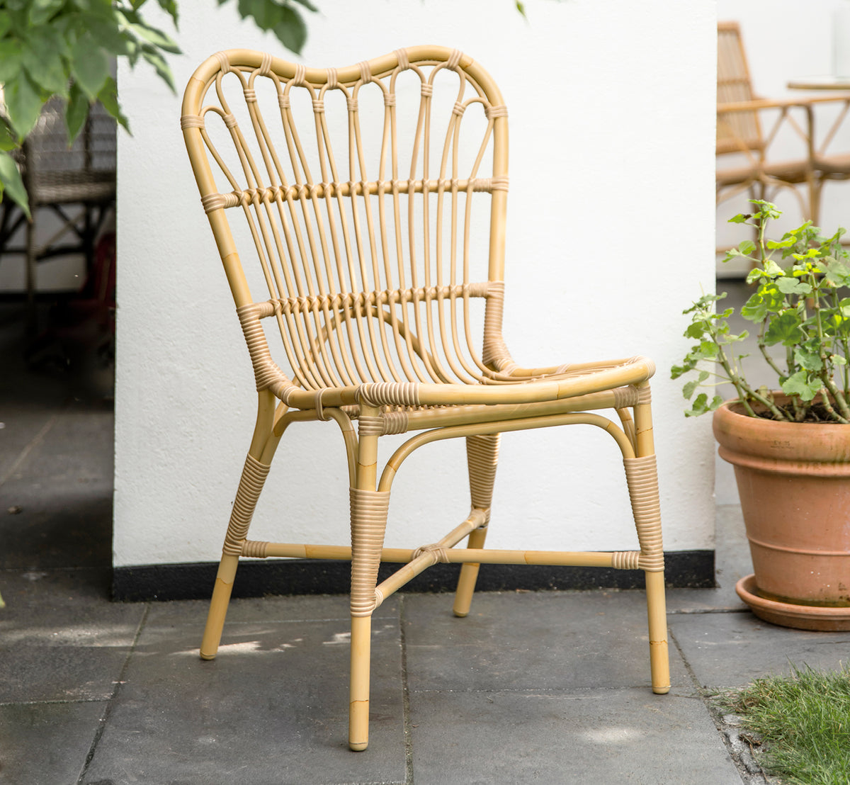 This is a lifestyle image of Margret Exterior Side Chair in natural aluminium artfibre. White courtyard with terracotta pots and plants.