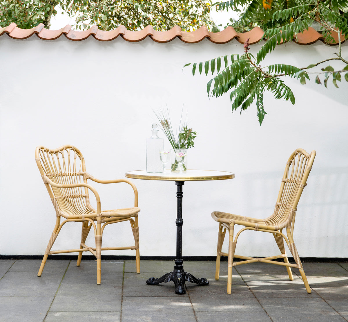 This is a lifestyle image of Margret Exterior Side Chair in natural aluminium artfibre. Courtyard with café table under tiled roof overhang.