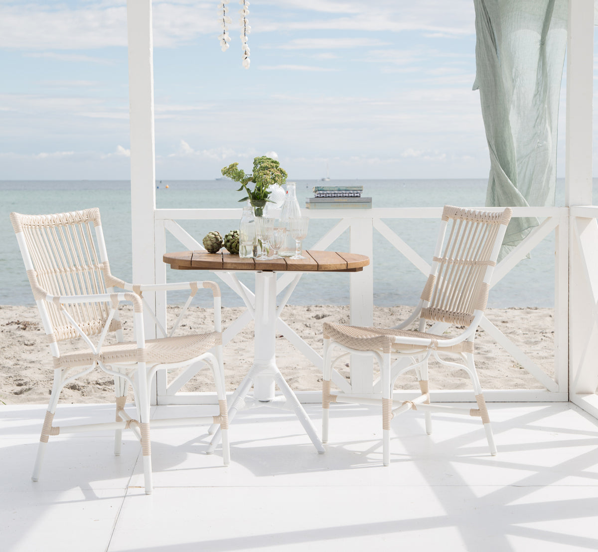 This is a lifestyle image of Piano Exterior Side Chair in dove white aluminium artfibre. At a seaside pergola dining area.