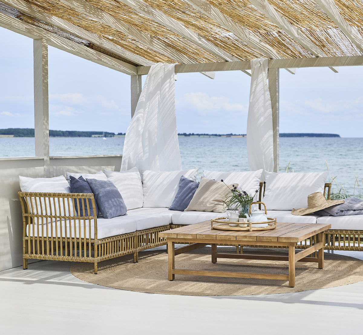 This is a lifestyle image of Maggie Sofa Corner Module in antique aluminium artfibre. Beach pavilion with sofa set and ocean view.