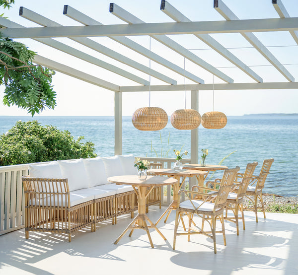 This is a lifestyle image of Meghan Exterior Dining Bench Corner Module in natural aluminium artfibre. On a seaside pergola terrace.