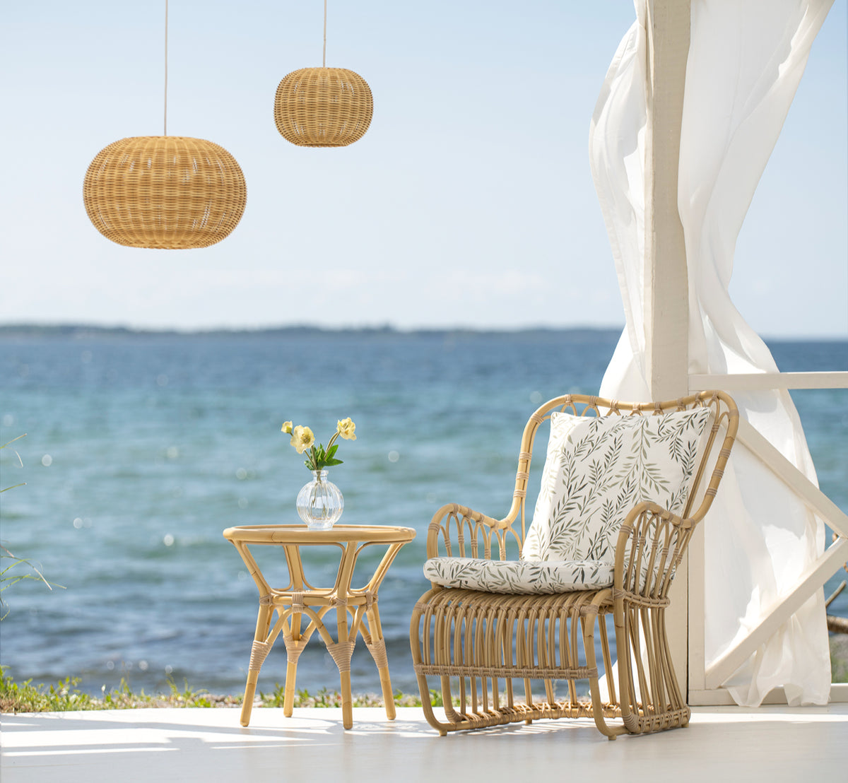 This is a lifestyle image of Tony Exterior Side Table in natural aluminium artfibre. Next to a lounge chair on a seaside deck.