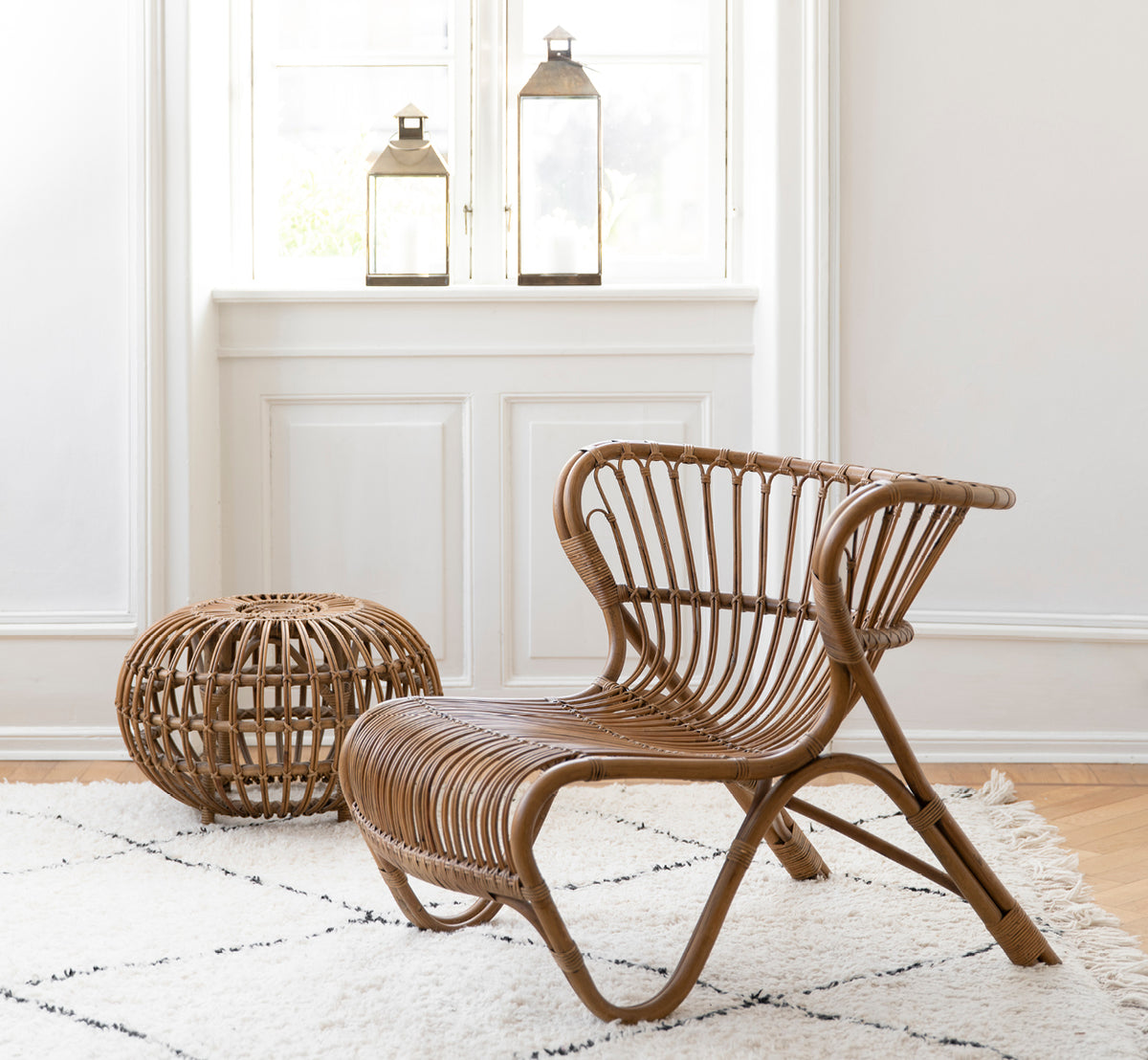 This is a lifestyle image of Fox Lounge Chair in polished Antique Rattan, in a warm interior with ochre wainscoting and dark herringbone parquet.