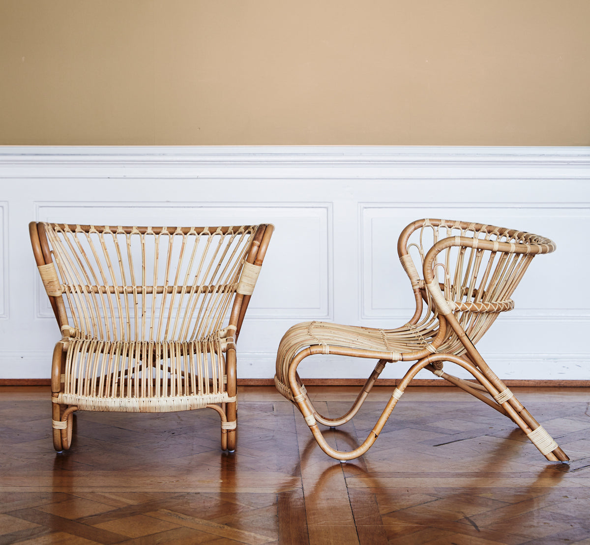 This is a lifestyle image of Fox Lounge Chair in polished Natural Rattan, in a warm interior with ochre wainscoting and dark herringbone parquet.