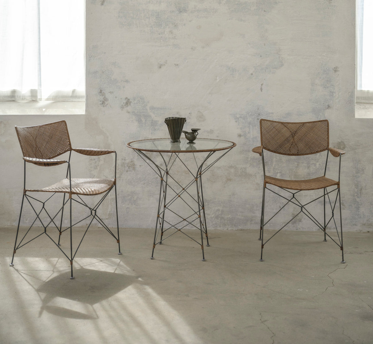 This is a lifestyle image of Rap Dining Chair in hazelnut rattan iron frame. With glass table in a pale, sunlit room.