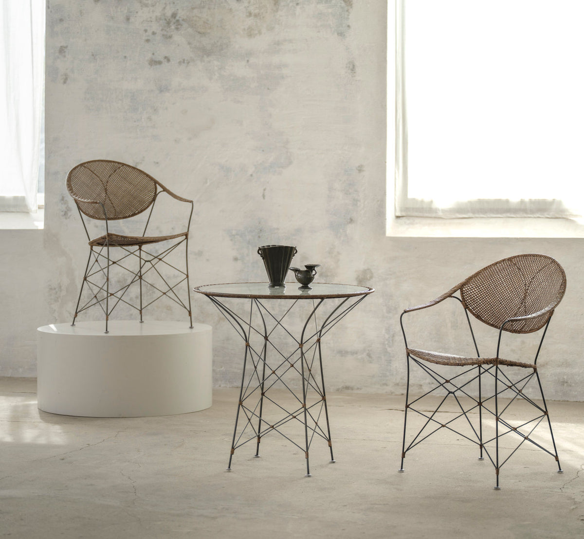 This is a lifestyle image of Funky Café Table in hazelnut rattan iron frame. With chairs and a plinth in a pale room.